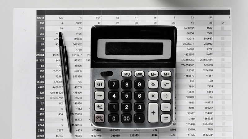 Kalkulator i olovka položeni na tabelu sa brojevima simbolizuju kako funkcioniše dvojno knjigovodstvo