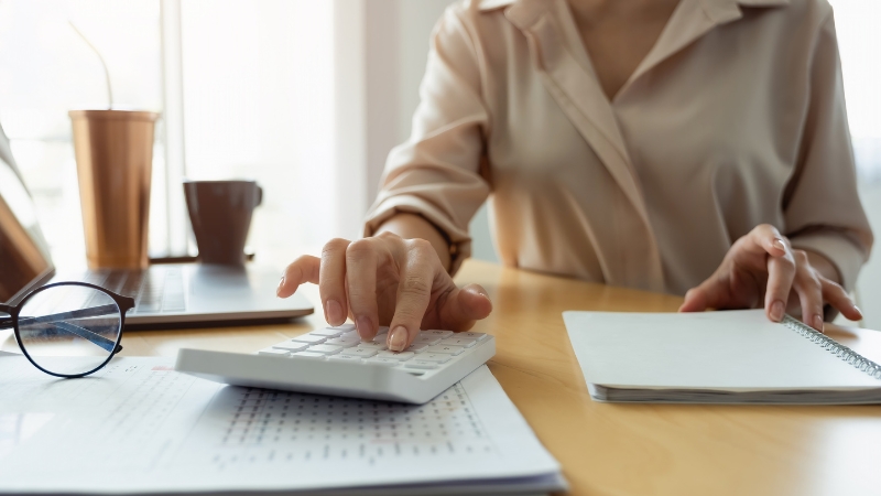 Knjigovođa koristi kalkulator i beležnicu dok proverava finansijske tabele