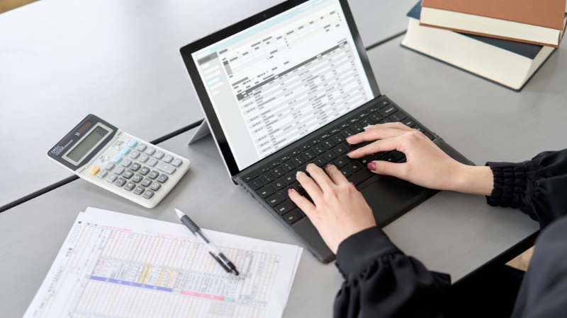 Osoba unosi podatke u računovodstveni program na laptopu uz kalkulator i tabele sa finansijskim izveštajima