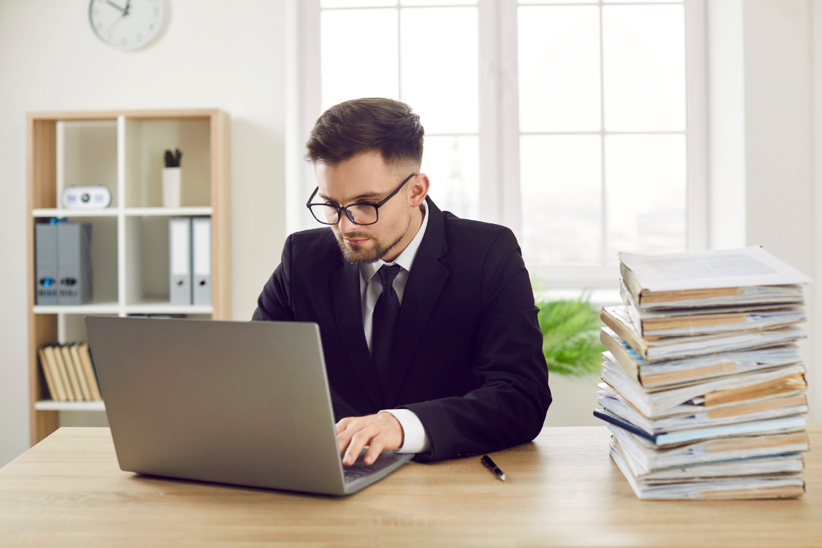 prikaz mladog preduzetnika koji koristi laptop, pored njega dokumenti